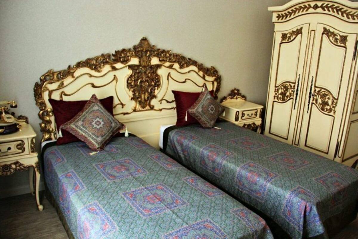 A room with a classic design, featuring a large ornate bed with a cream-colored headboard and matching nightstands. There is a matching wardrobe with decorative panels.