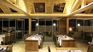 An indoor dining area with tables set for meals, large windows, and a high ceiling with decorative elements. - Kasr-ı Sercehan Hotel (Nusaybin)