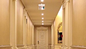 A long, narrow hallway with ornate white railings and a polished floor, leading to a door with intricate designs. - Kasr-ı Sercehan Hotel (Nusaybin)