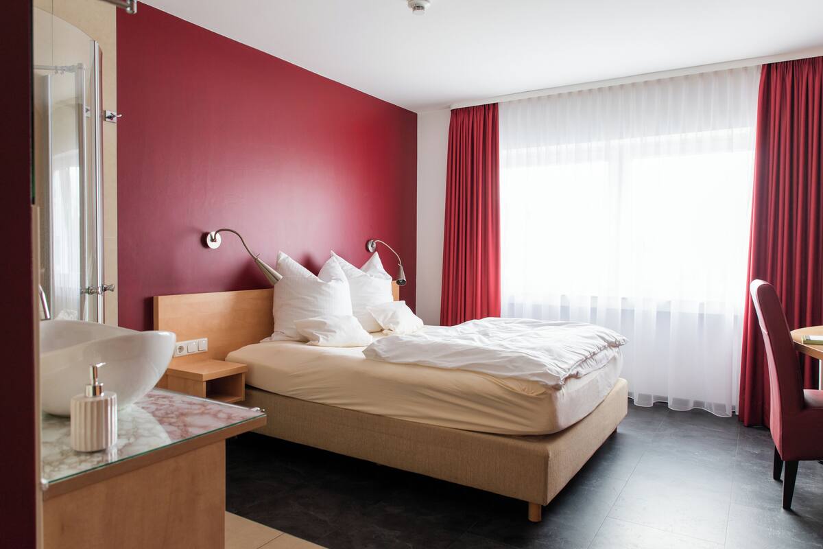 Ein Hotelzimmer mit Bett, Nachttisch und einem Badezimmer mit Waschbecken und Spiegel.