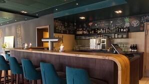 Een bar met een houten toonbank, smaragdgroene barstoelen en een krijtbordmenu.