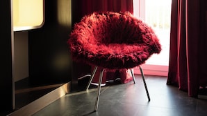 Een moderne kamer met een rode stoel, een donkere vloer en een raam met gordijnen.
