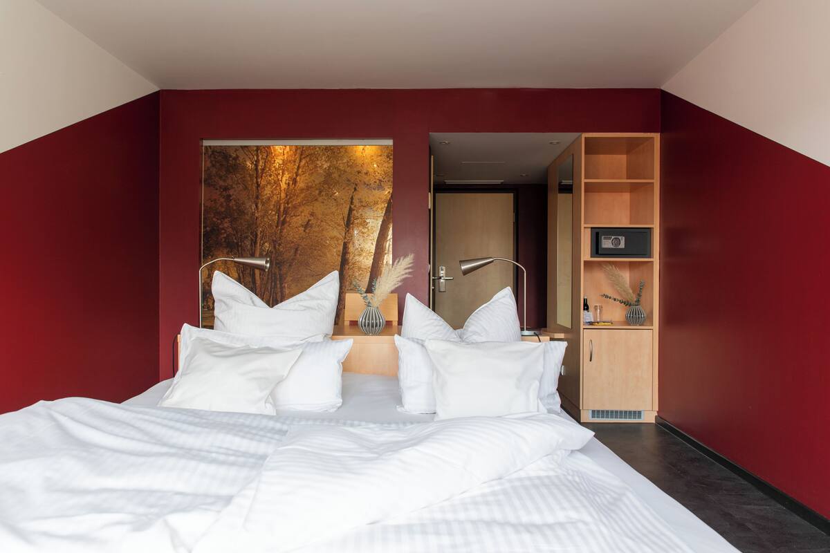 Ein modernes Schlafzimmer mit einem großen Bett, einem Spiegel, einem Holzkasten und einem Baumgemälde.