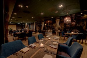 Un restaurante espacioso con varias mesas preparadas para comer, con velas y copas de vidrio transparente.