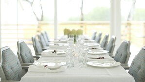Una mesa de comedor dispuesta con platos, vasos y cubiertos, con sillas a cada lado.