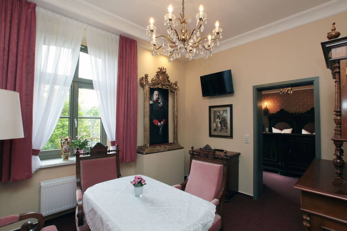 Ein Zimmer mit Esstisch, Stühlen, einer Kristallleuchter, einem Kamin und einem Fernseher.