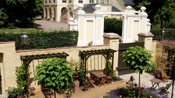 Een binnenplaats met terras, een groot gebouw op de achtergrond en een verzorgde tuin.