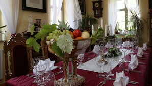 Een elegante eetzaal met een gedekte tafel, inclusief een fruitschaal, wijnglazen en een klok aan de muur.