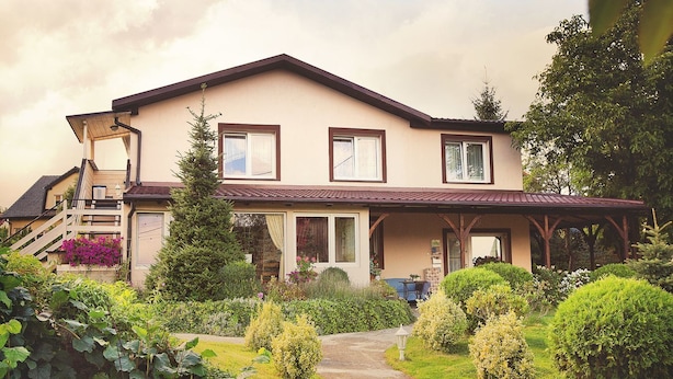 Een tweelaags huis met een overdekte veranda, een voortuin en een trap naar de ingang.