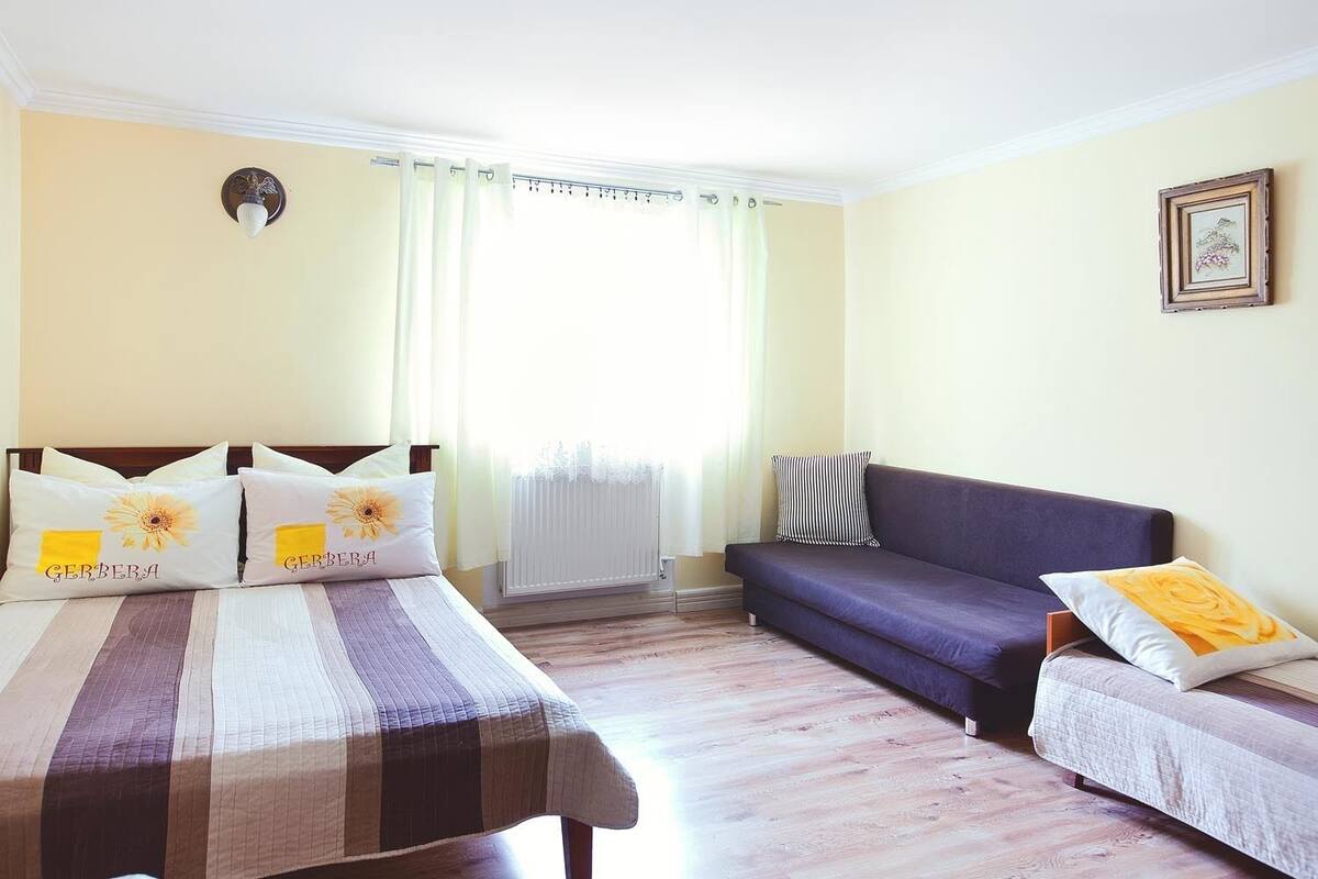 Une chambre à coucher avec un lit, deux tables de chevet, un canapé et une fenêtre avec des rideaux.