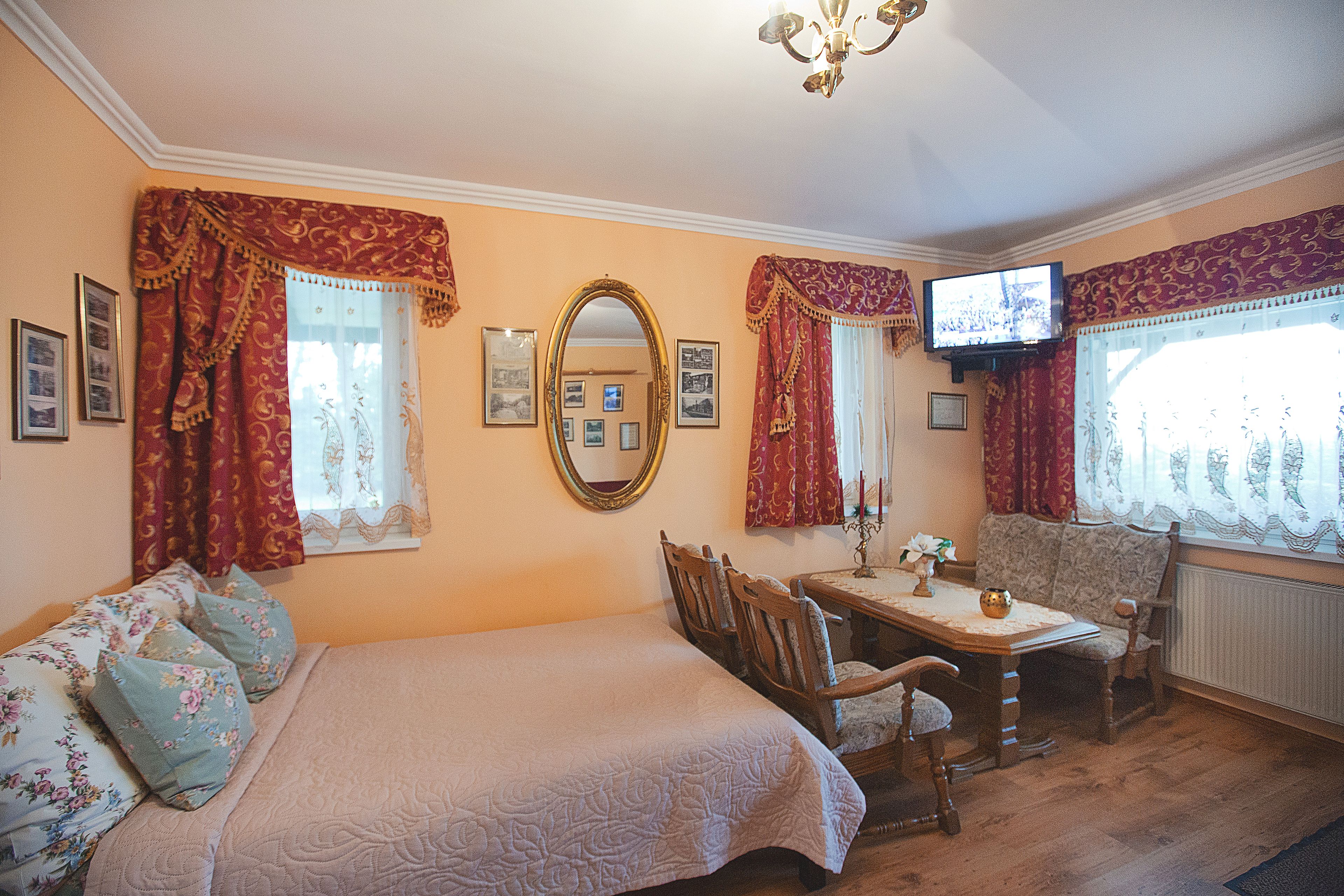 Una habitación con cama, una mesa con sillas, televisión y ventana con cortinas.