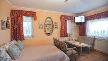 Quarto com cama, mesa e cadeiras, televisão e janela com cortinas.