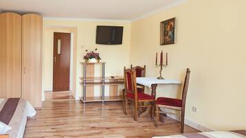Una stanza con pavimento in legno, un letto con lenzuola a righe, un armadio in legno, un tavolo da pranzo con sedie, una televisione a parete e un quadro.