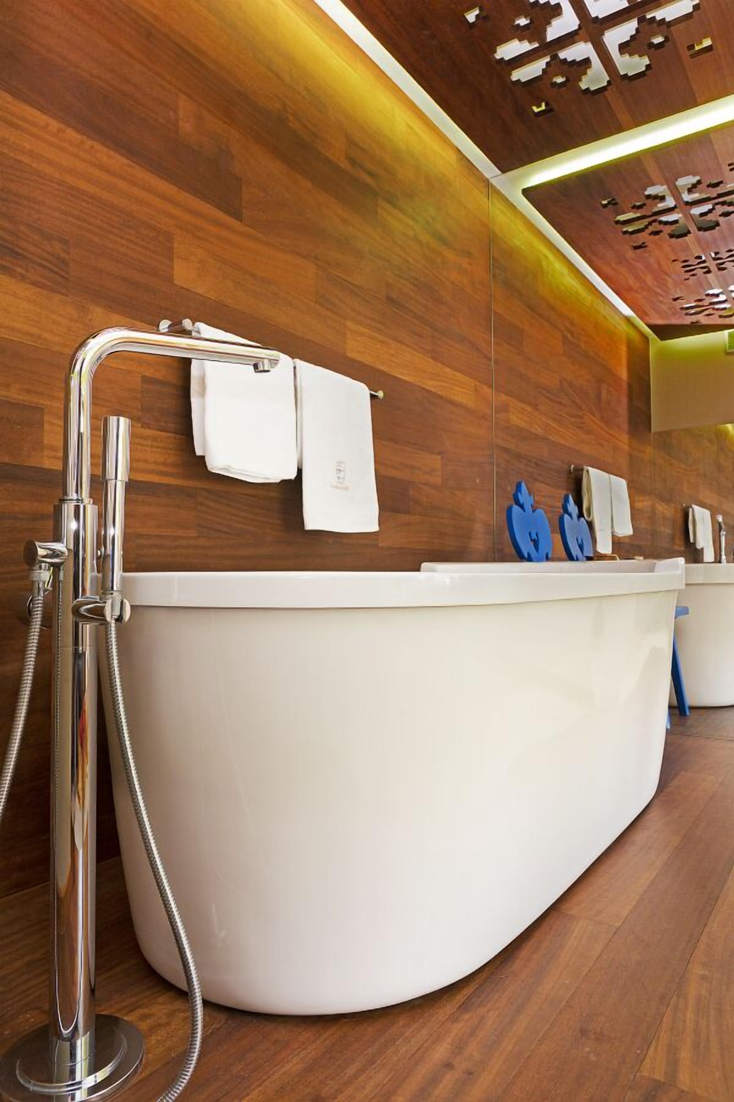 Un baño moderno con una bañera independiente, un cabezal de ducha y una pared de madera con diseño geométrico.