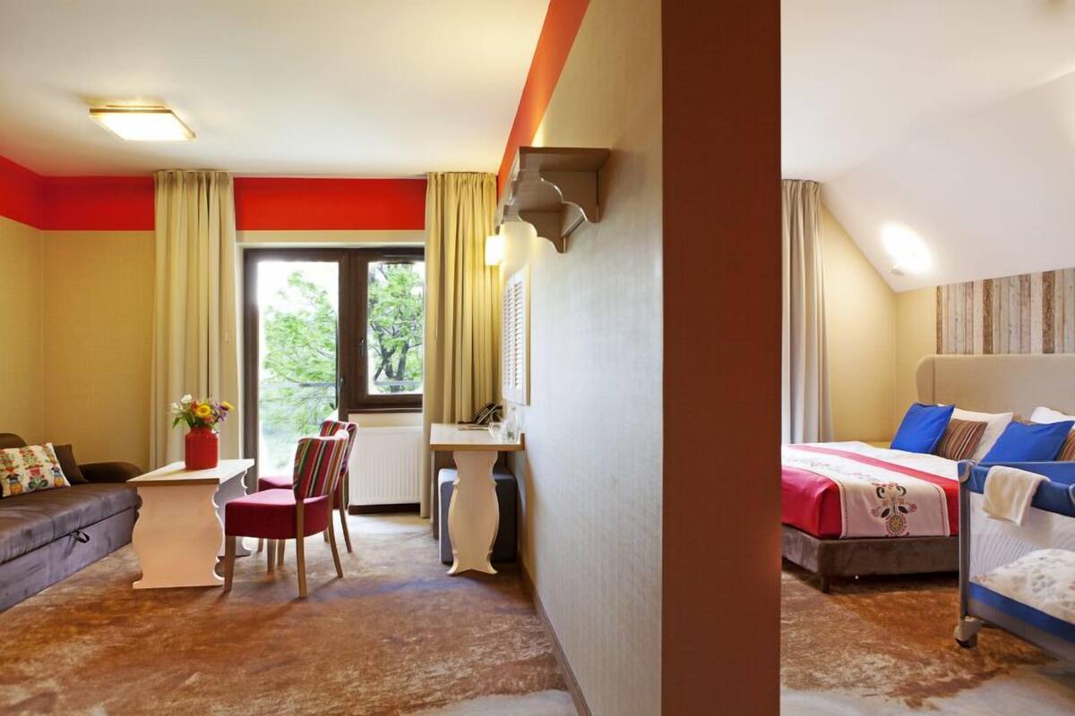 A hotel room with a bed, a desk, a chair, a sofa, and a window with curtains.
