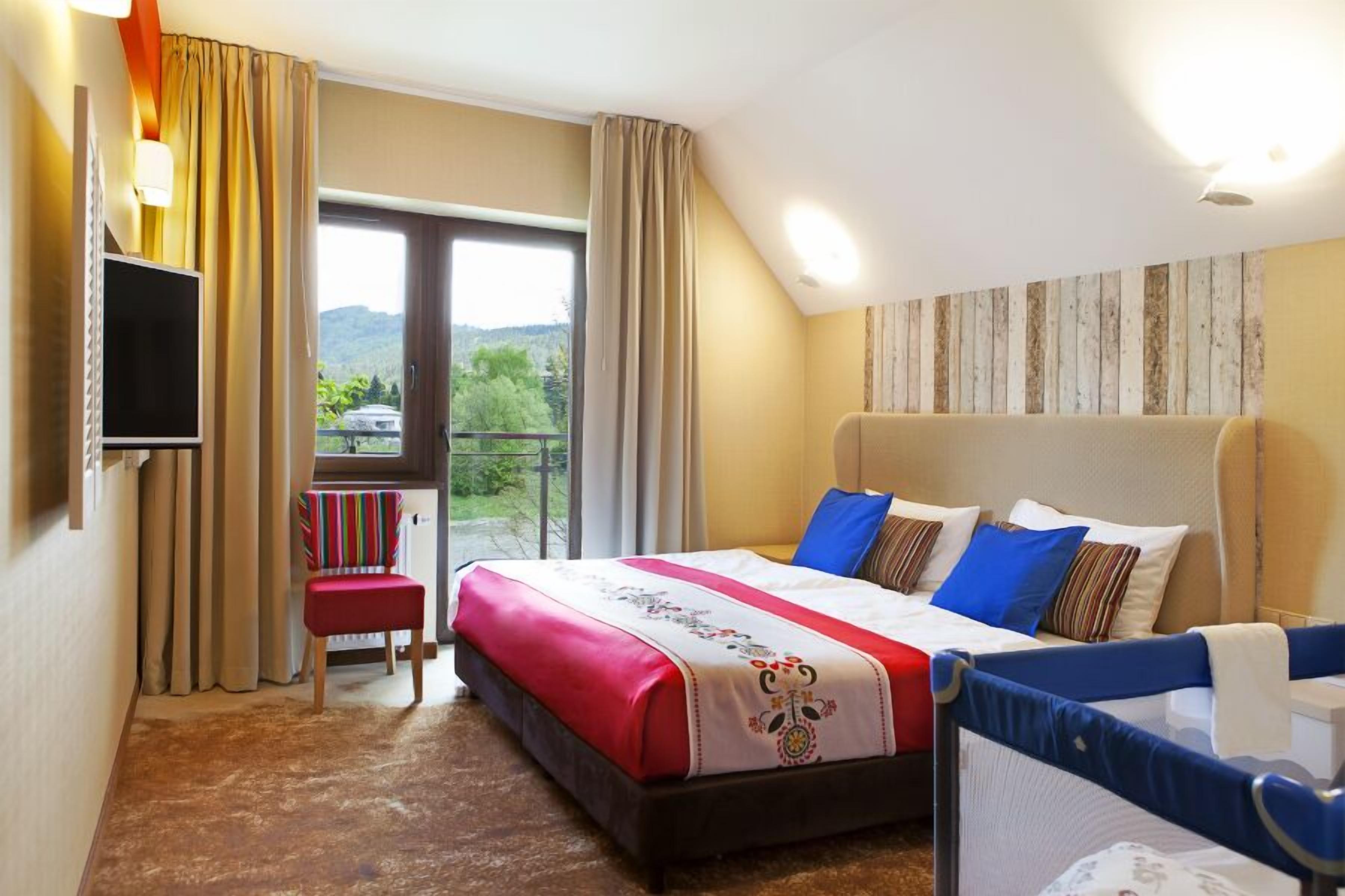 Habitación de hotel con una cama grande, televisión, silla y balcón con vistas a la vegetación.
