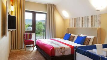 Habitación de hotel con una cama grande, televisión, silla y balcón con vistas a la vegetación.