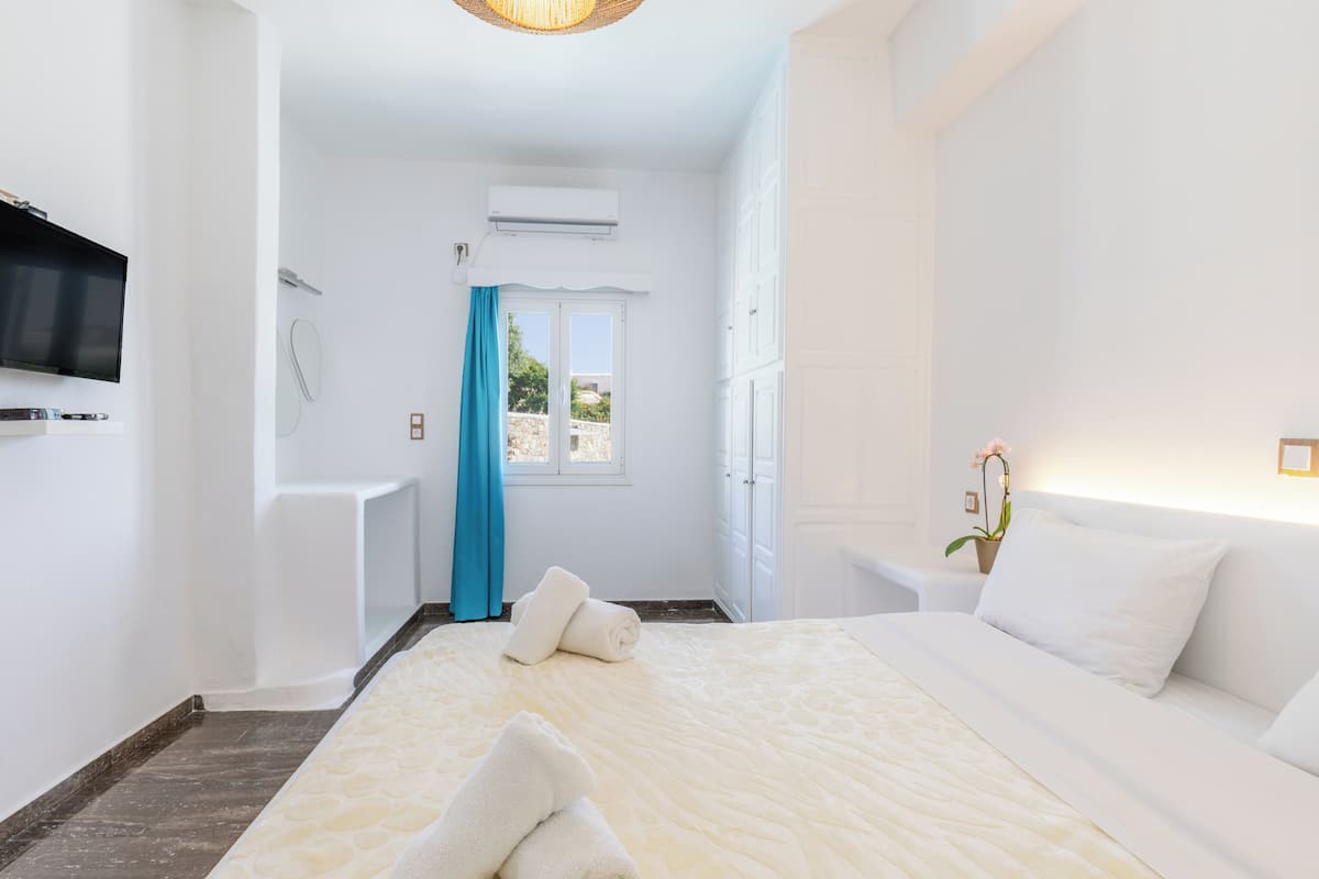 Relax in a spacious room with a large bed, flat-screen TV, and air conditioning unit, offering a clean and uncluttered space with a view of the outdoors.