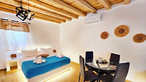 A modern bedroom with a bed, bedside table, and a dining area with chairs and a table. - Mykonian Breeze (Mykonos)