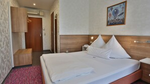 A hotel room with a neatly made bed, a bedside table with a phone, a nightstand, a wooden headboard, and a wall-mounted air conditioner. - Hotel Am Bismarck (Mannheim)