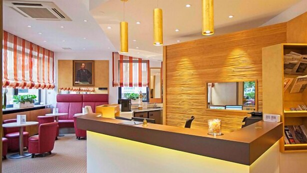 A modern hotel lobby with a reception desk, seating area, and a large window with curtains. - Hotel Am Bismarck (Mannheim)