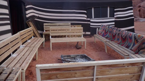 A rustic outdoor seating area with wooden benches and a colorful blanket. - Wadi Rum Safari Camp (Wadi Rum)