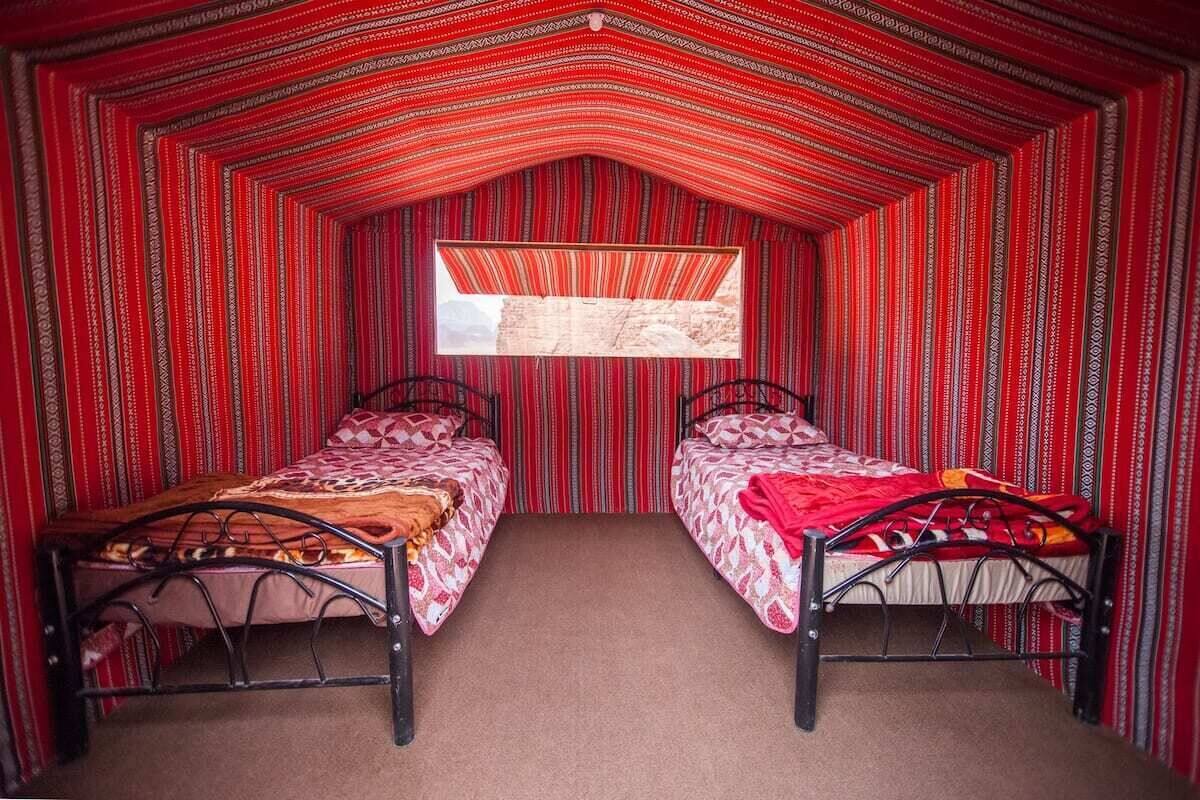A small, cozy room with two beds, a window, and a striped red and white wall pattern.