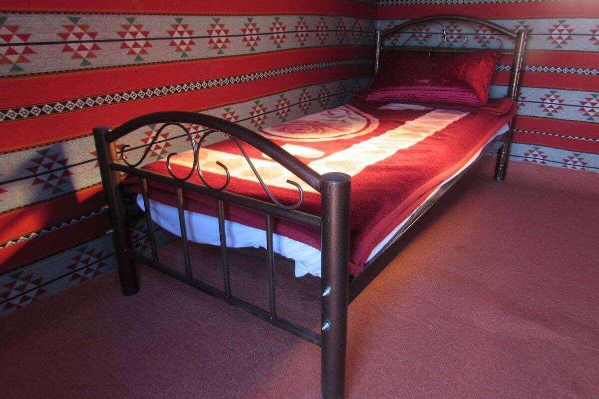 A single bed with a metal frame and a red blanket in a room with patterned walls.