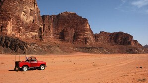 A red car parked on a desert road with rock formations in the background. - Wadi Rum Safari Camp (Wadi Rum)