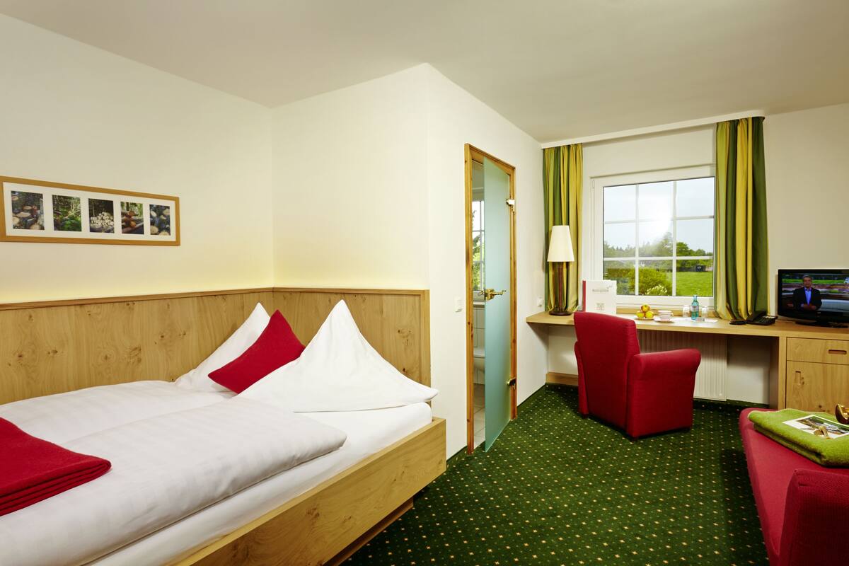 A hotel room with a wooden bed, a desk with a computer, a chair, and a TV.