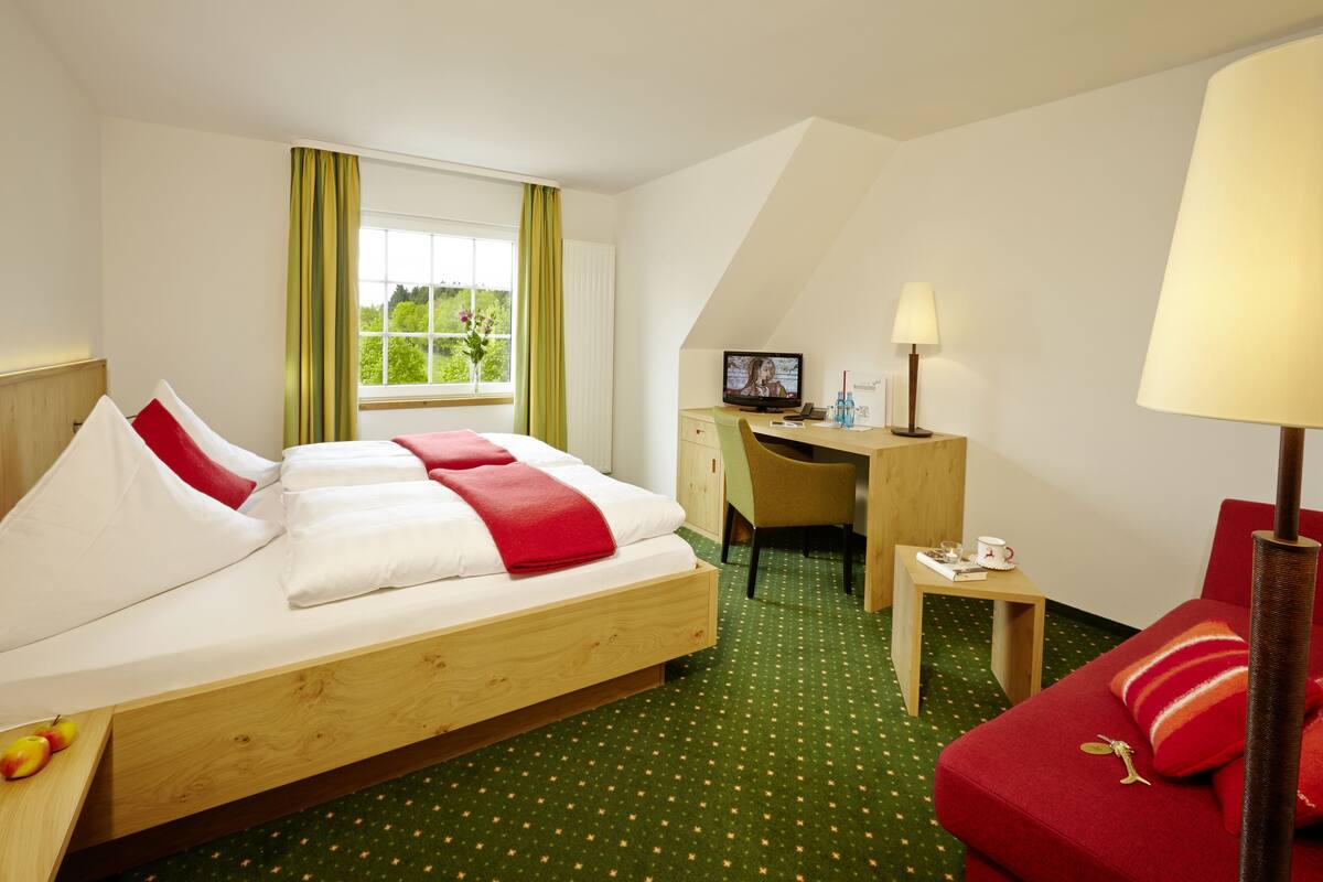 A hotel room with a bed, a desk, a chair, a lamp, and a sofa.