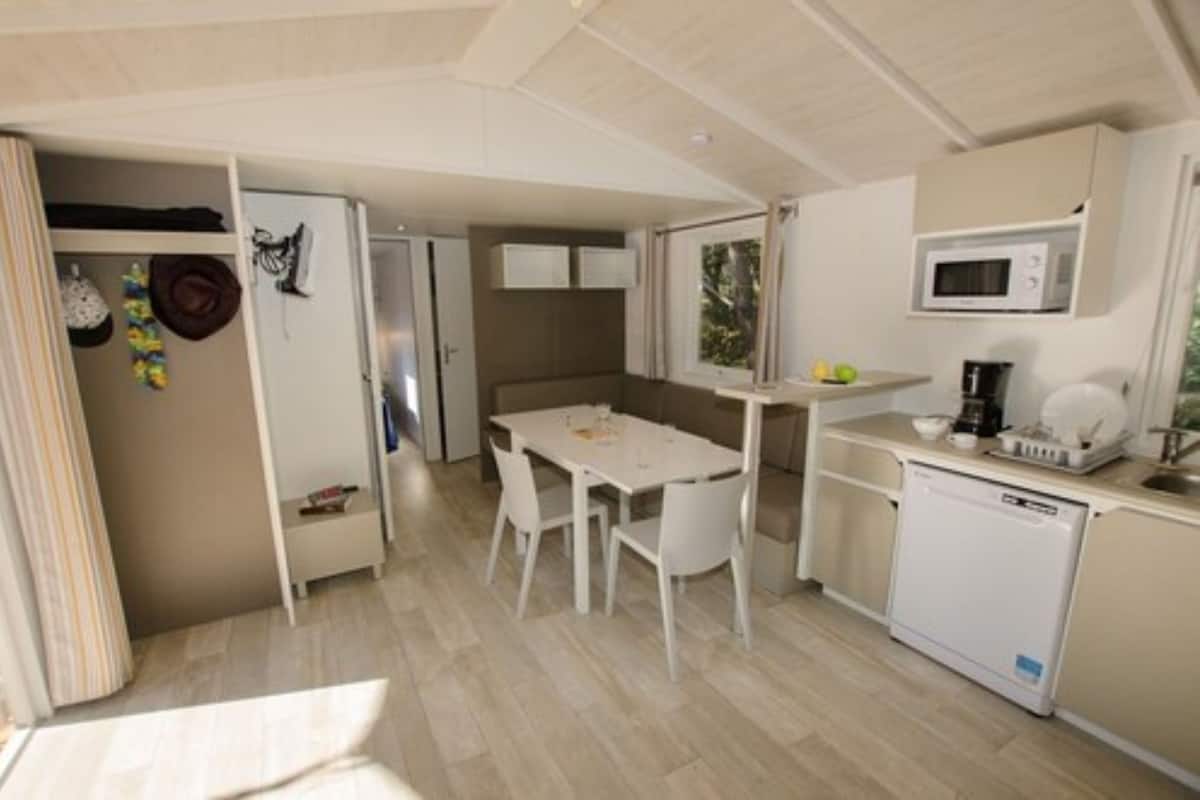 Una cocina compacta con mesa de comedor, sillas blancas, microondas y lavavajillas.