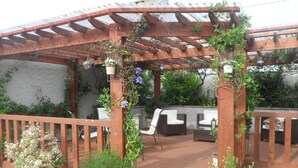 A wooden pergola with a tiled roof, surrounded by potted plants and outdoor furniture. - Midtown Farm Bed & Breakfast (Wigton)