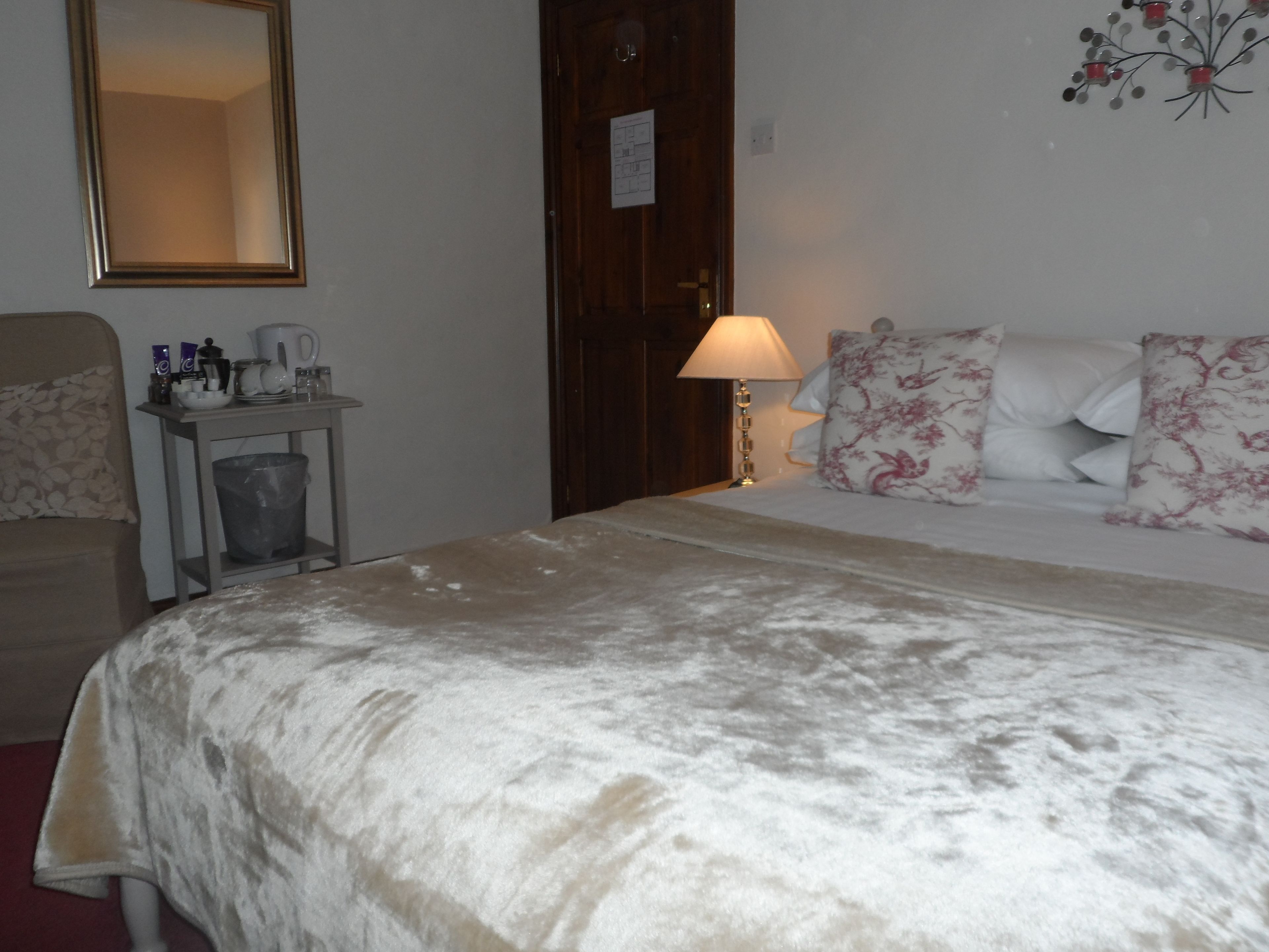 A hotel room with a bed, a nightstand, a lamp, a mirror, and a wall decoration.