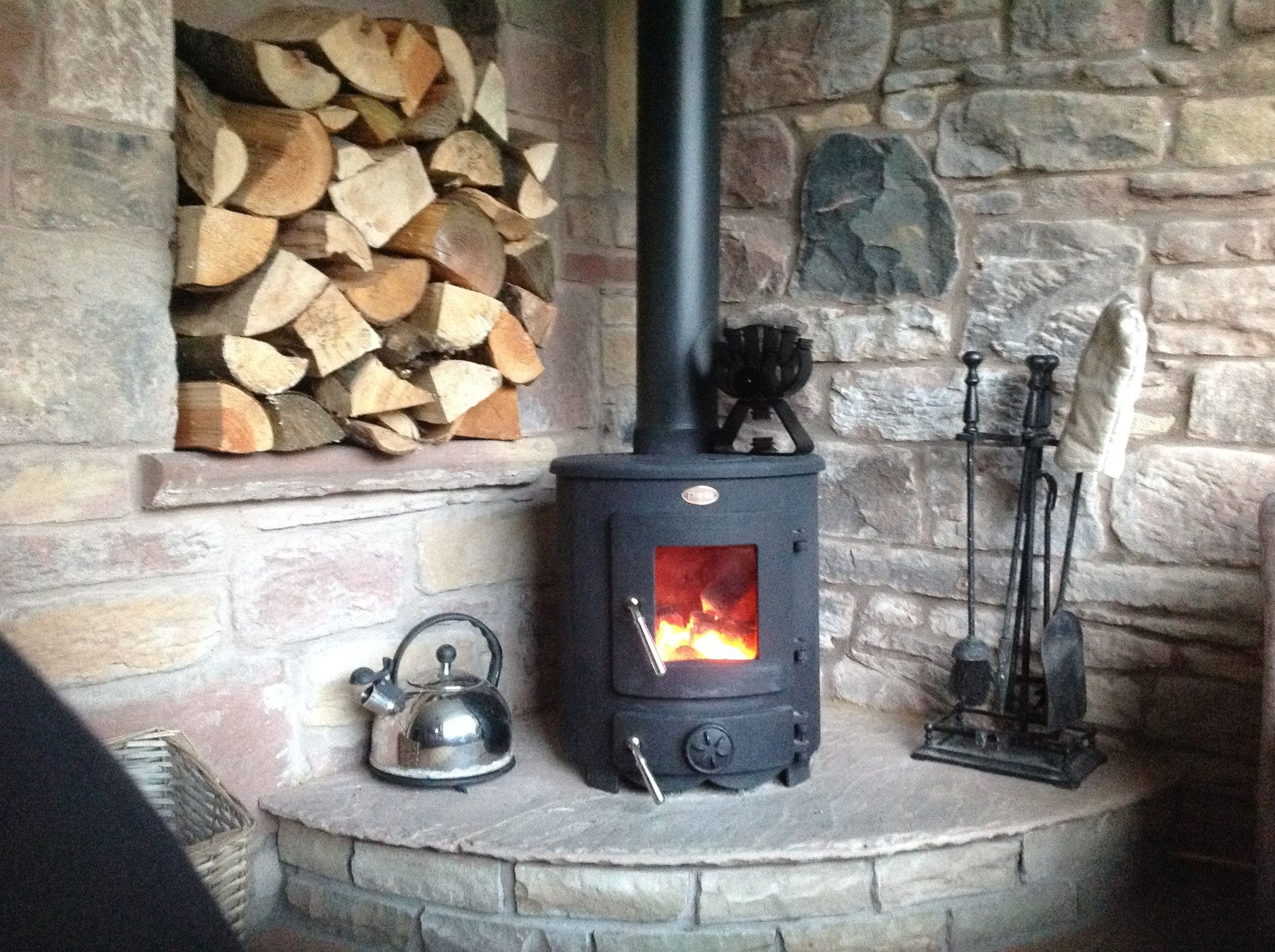 A stone fireplace with a wood stove, a kettle, and a candle holder.