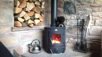 A stone fireplace with a wood stove, a kettle, and a candle holder.
