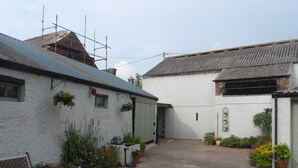 A narrow courtyard with white buildings, a bench, potted plants, and a metal roof. - Midtown Farm Bed & Breakfast (Wigton)