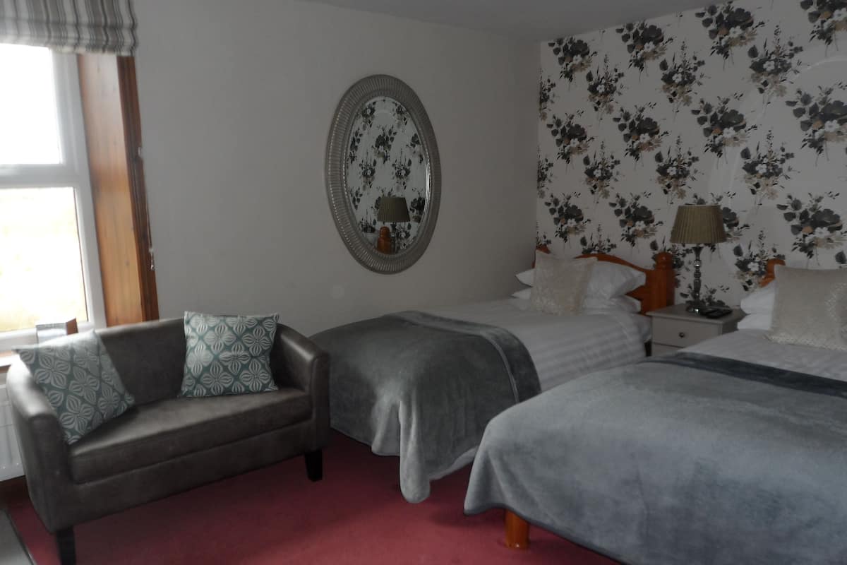 A bedroom with two beds, a sofa, a mirror, and floral wallpaper.