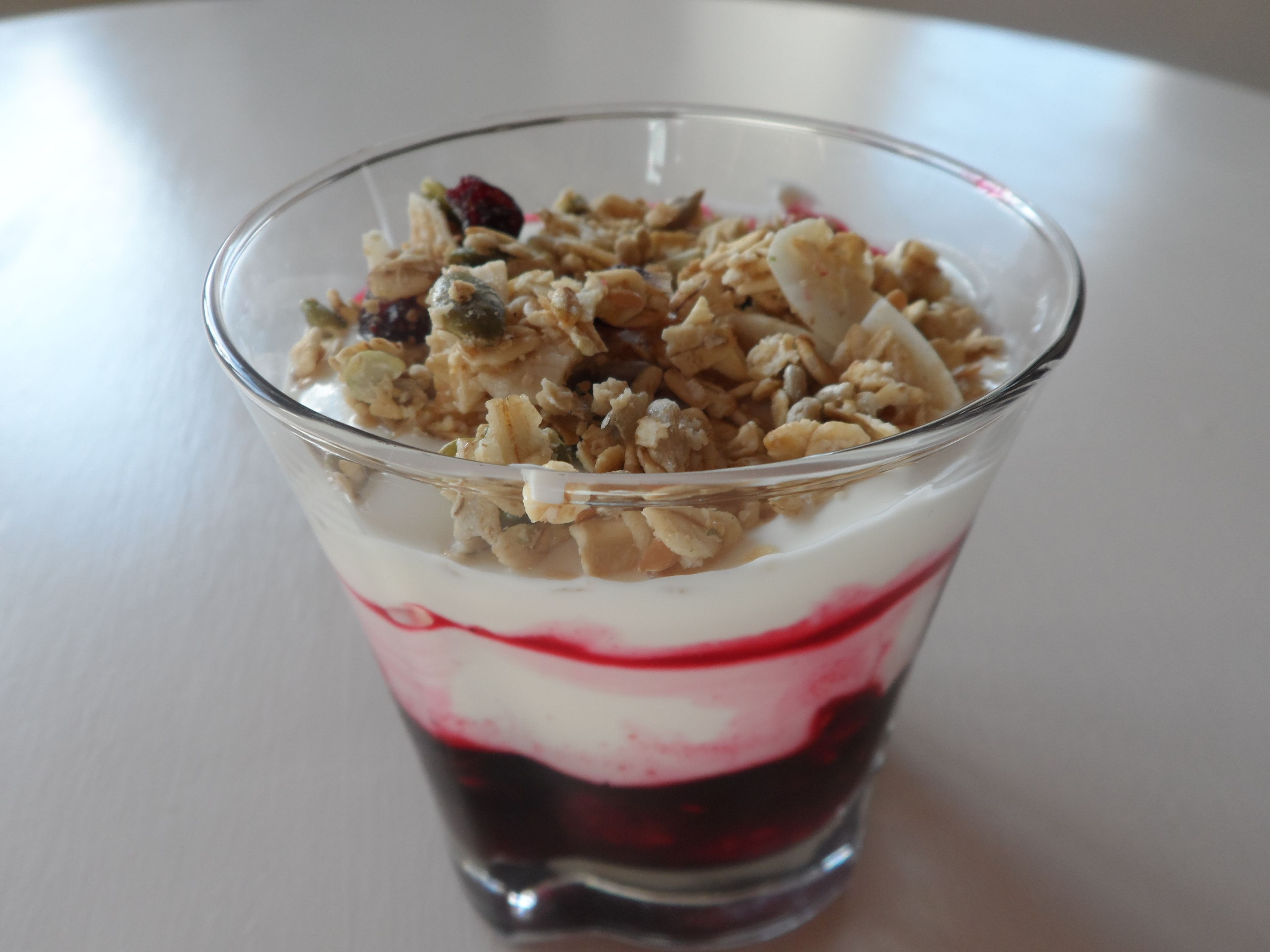 A glass dessert with layers of granola, yogurt, and red fruit compote.