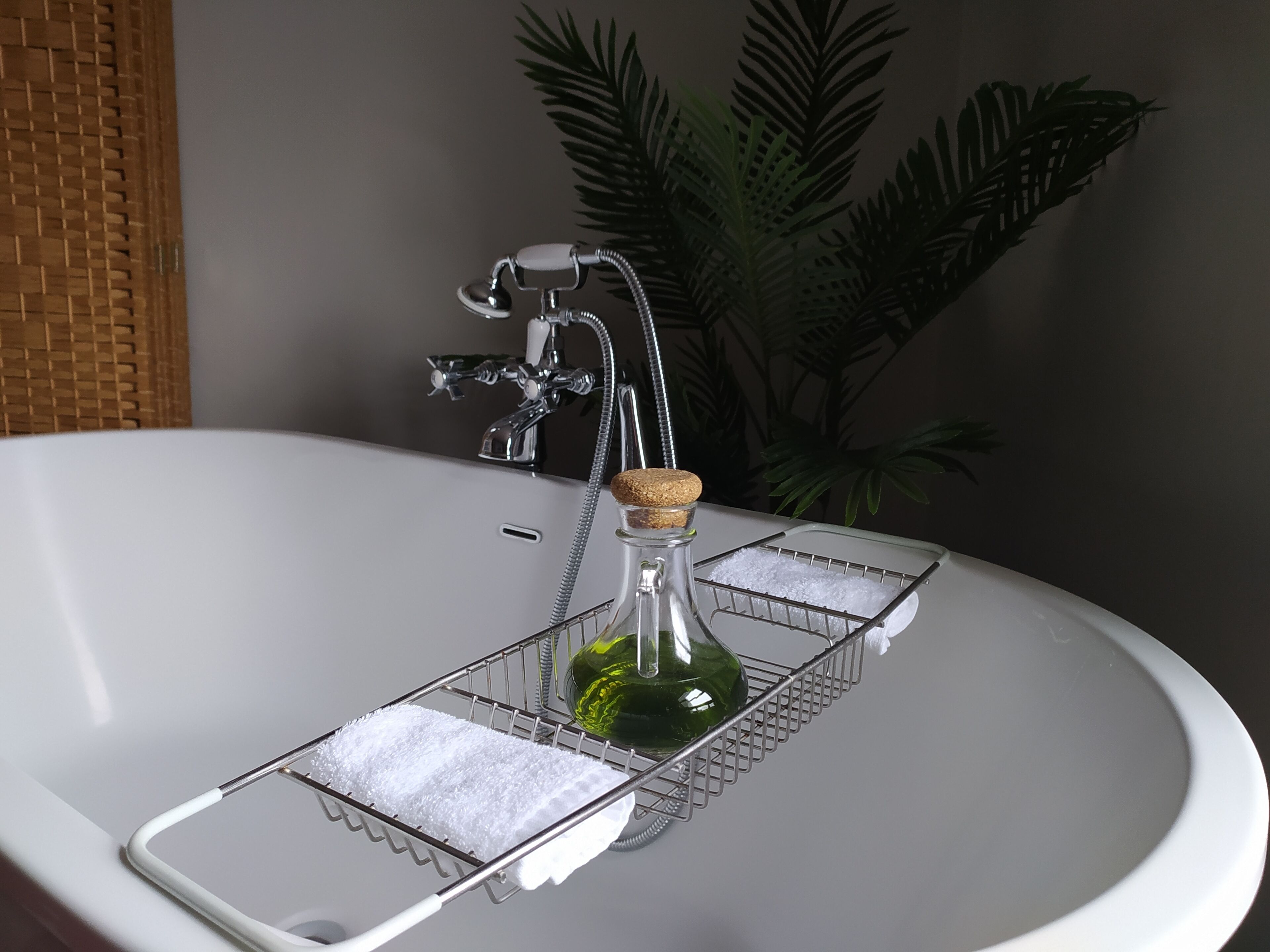 Ein Badezimmer mit Waschbecken in Weiß, einem Chrom-Wasserhahn, einer Glasflasche mit Korkverschluss und einem Tablett mit Handtuch.