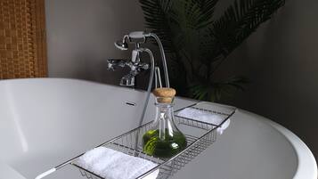 Ein Badezimmer mit Waschbecken in Weiß, einem Chrom-Wasserhahn, einer Glasflasche mit Korkverschluss und einem Tablett mit Handtuch.
