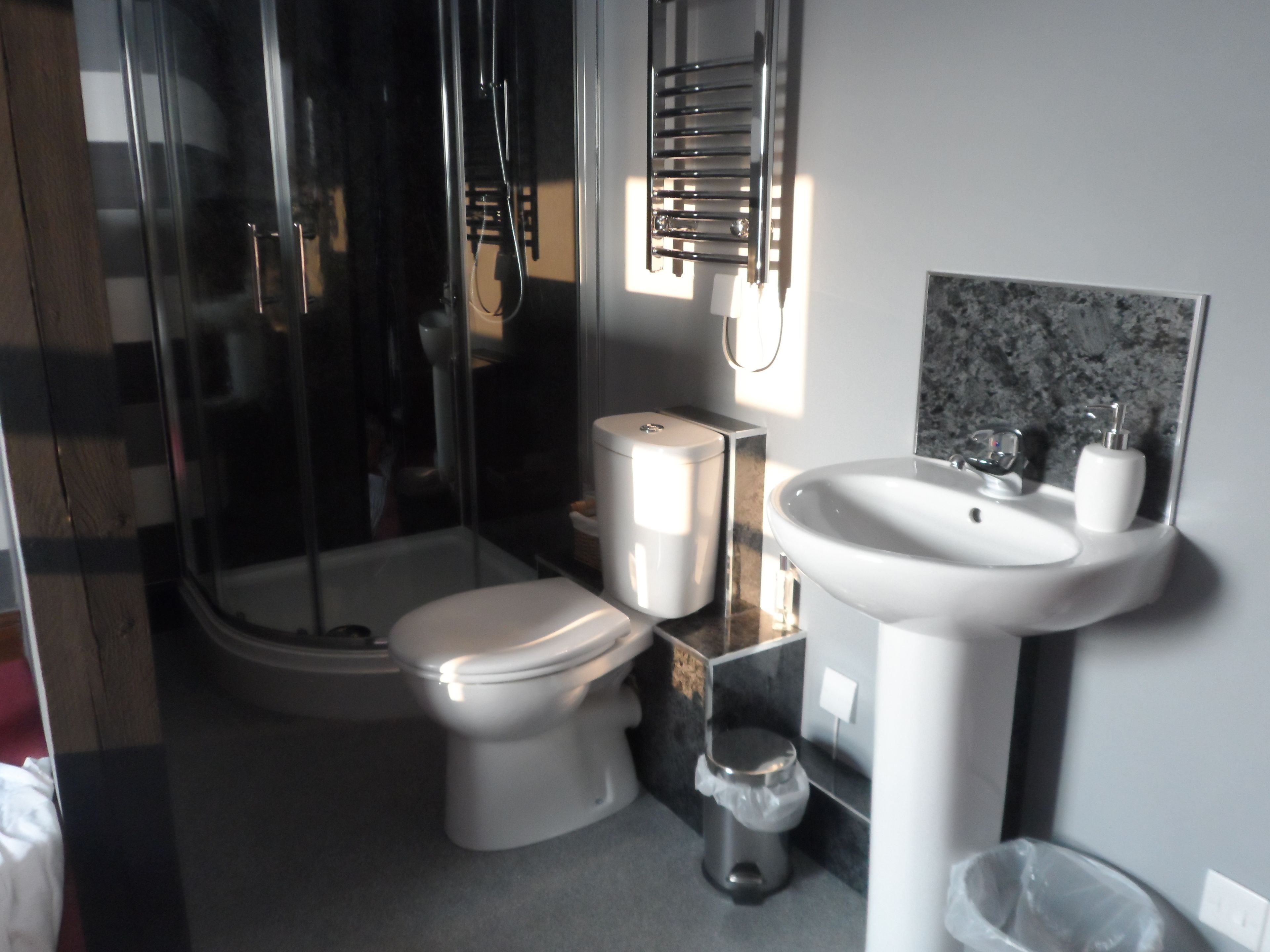 A modern bathroom with a glass shower enclosure, a toilet, a sink, and a marble backsplash.