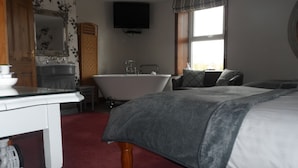 A bedroom with a large bed, a bathtub, a television, and a wooden cabinet. - Midtown Farm Bed & Breakfast (Wigton)