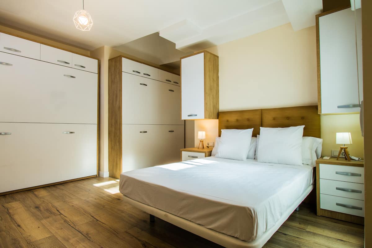 A hotel room with a large bed, wooden flooring, built-in wardrobes, and bedside tables with lamps.
