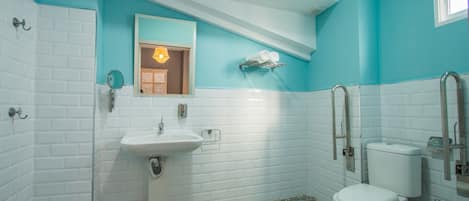 A bathroom with white subway tiles, a white sink, a toilet, and a shower area.