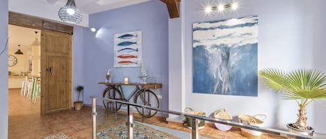 A hallway with a wooden door, a dining area with chairs, a bicycle, and a large painting of a wave.