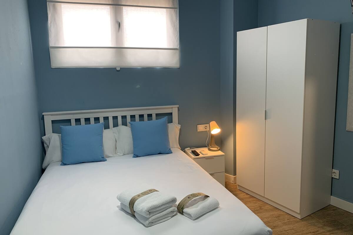 A bedroom with a bed, pillows, a nightstand, a lamp, and a wardrobe.