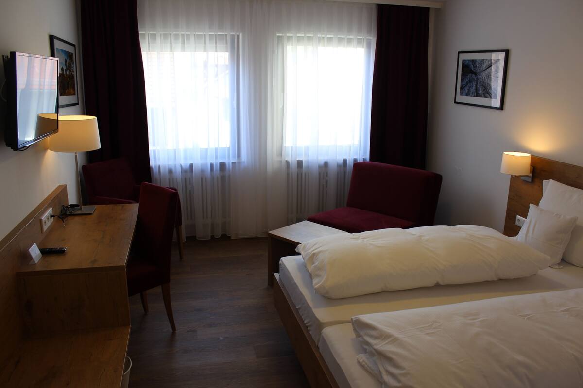 Une chambre d’hôtel avec un bureau en bois, deux chaises rouges, un lit avec une literie blanche et un téléviseur fixé au mur.