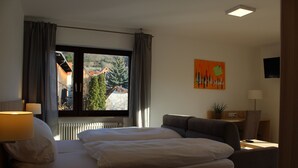Hotelkamer met een bed, een bureau, een stoel, een lamp en een raam met uitzicht op gebouwen en bomen.