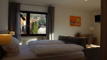 Ein Hotelzimmer mit einem Bett, einem Schreibtisch, einem Stuhl, einer Lampe und einem Fenster mit Blick auf Gebäude und Bäume.